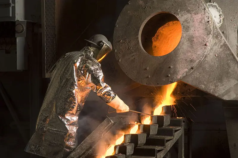 Worker in heat-resistant suit pouring molten gold into bar molds at a gold mine